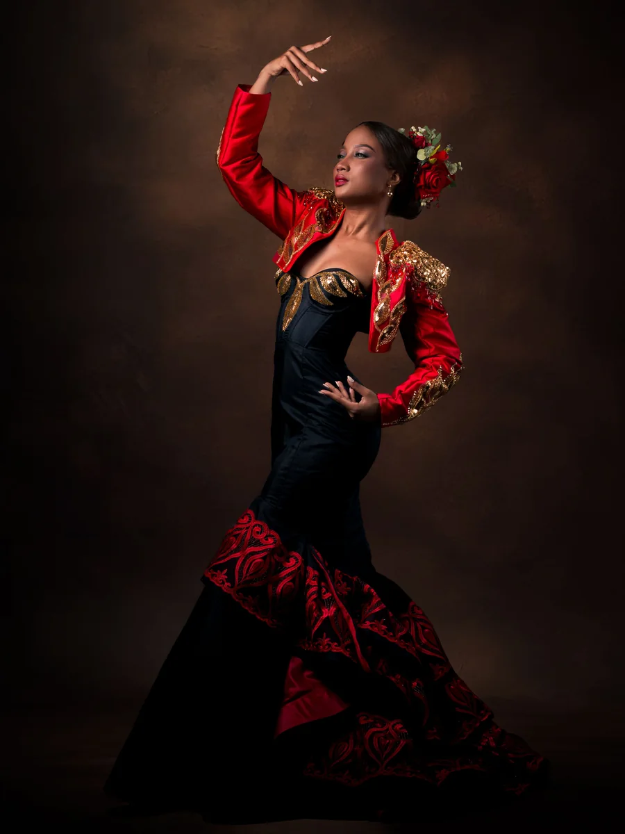 A flamenco dancer in a red and black dress mid-pose, one arm raised, against a dark studio background (representative photograph, not Corral de la Morería's own cast)