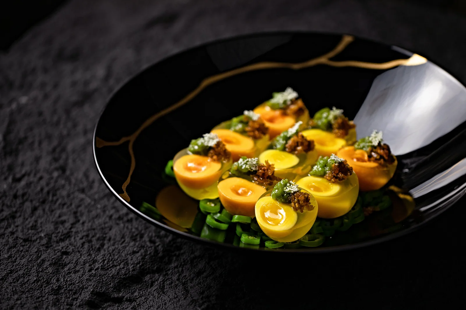 A precisely plated modern dish on a black plate against a dark slate surface (representative photograph of contemporary tasting-menu cooking, not Corral de la Morería's own kitchen)