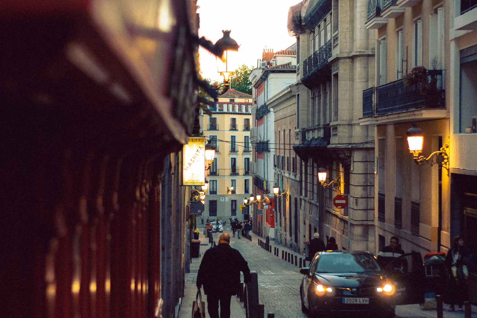 A cobbled old-town Madrid street at dusk, lit by wall lanterns (representative photograph of Madrid's historic centre, not the Morería itself)
