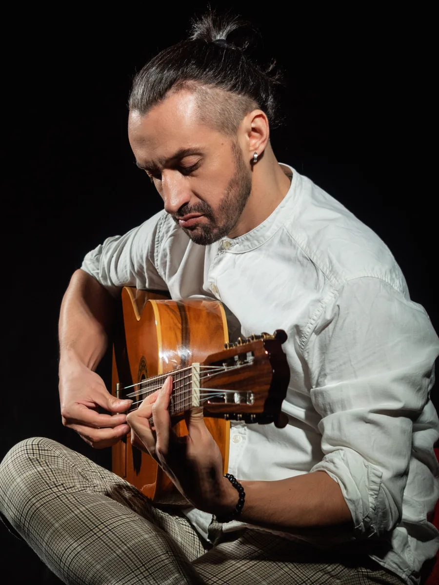 A flamenco guitarist playing a classical guitar, lit against a black background (representative photograph, not Corral de la Morería's own cast)
